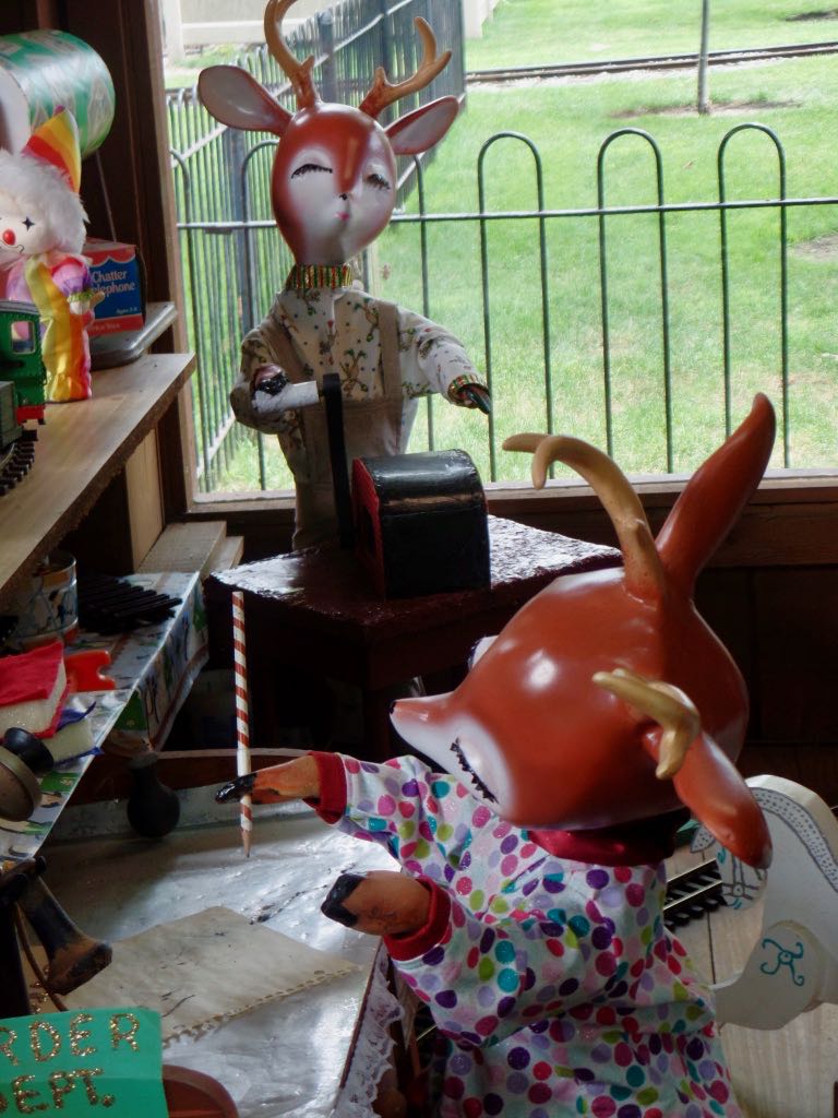Reindeer at Santa's Workshop in Story Book Land. One holds a pencil and makes notes. The other is at the adding machine. Both are dressed in office-casual pajamas.