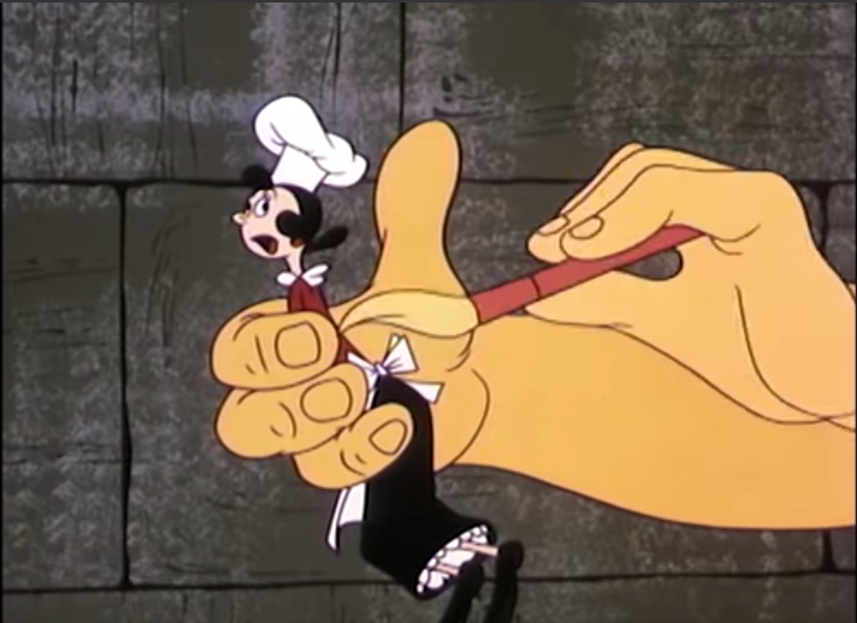 Olive Oyl, dressed as a cook, held in a giant hand while the other hand pai...