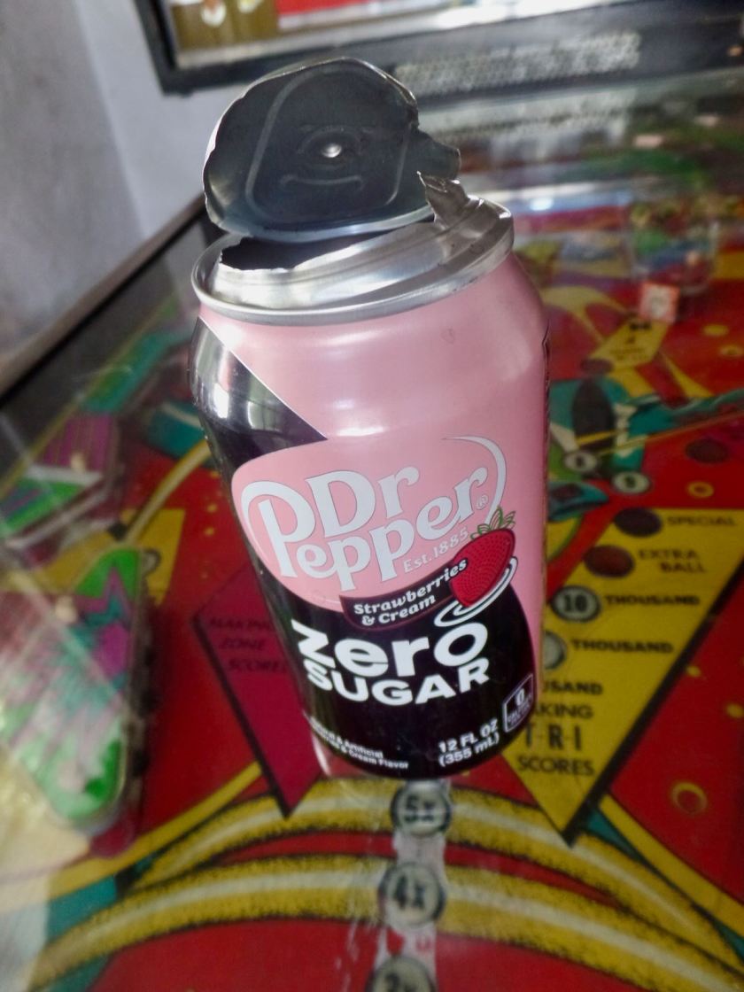 Photograph of an empty can of Dr Pepper, the lid of which has been ripped open and peeled outward without the tab having been opened, that is, so the can appears to have been exploded from within.